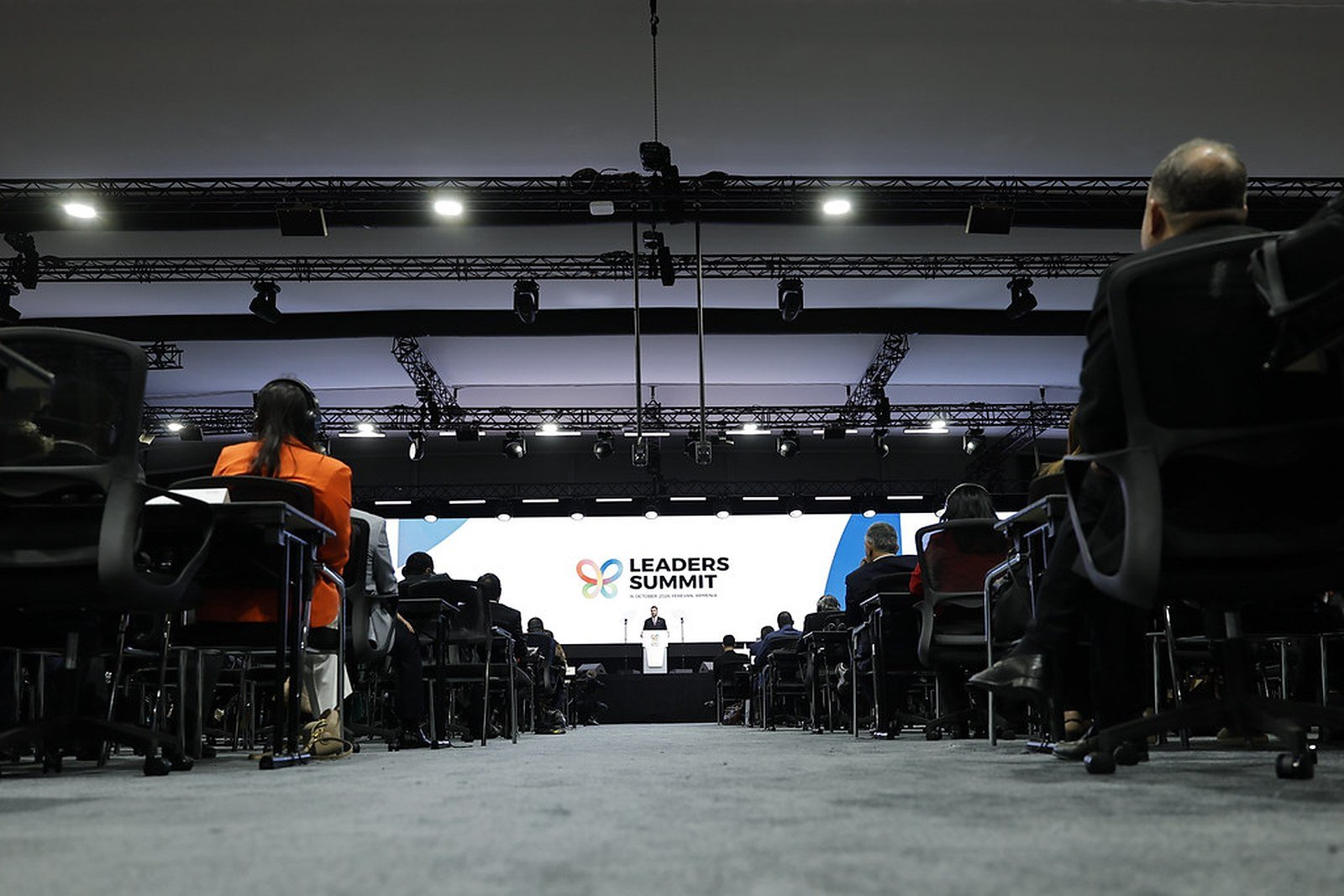 A speaker at the podium on the stage of the COP17 Leaders' Summit in Yerevan, seen from among the delegates' seats, with the Leaders Summit screen behind