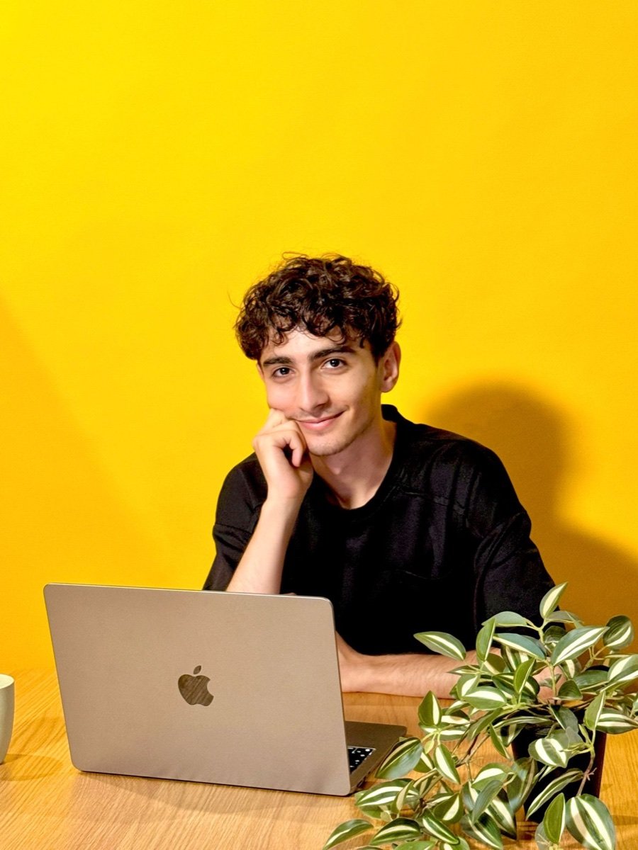 Portrait of Narek Ohanyan seated at a laptop against a bright yellow backdrop