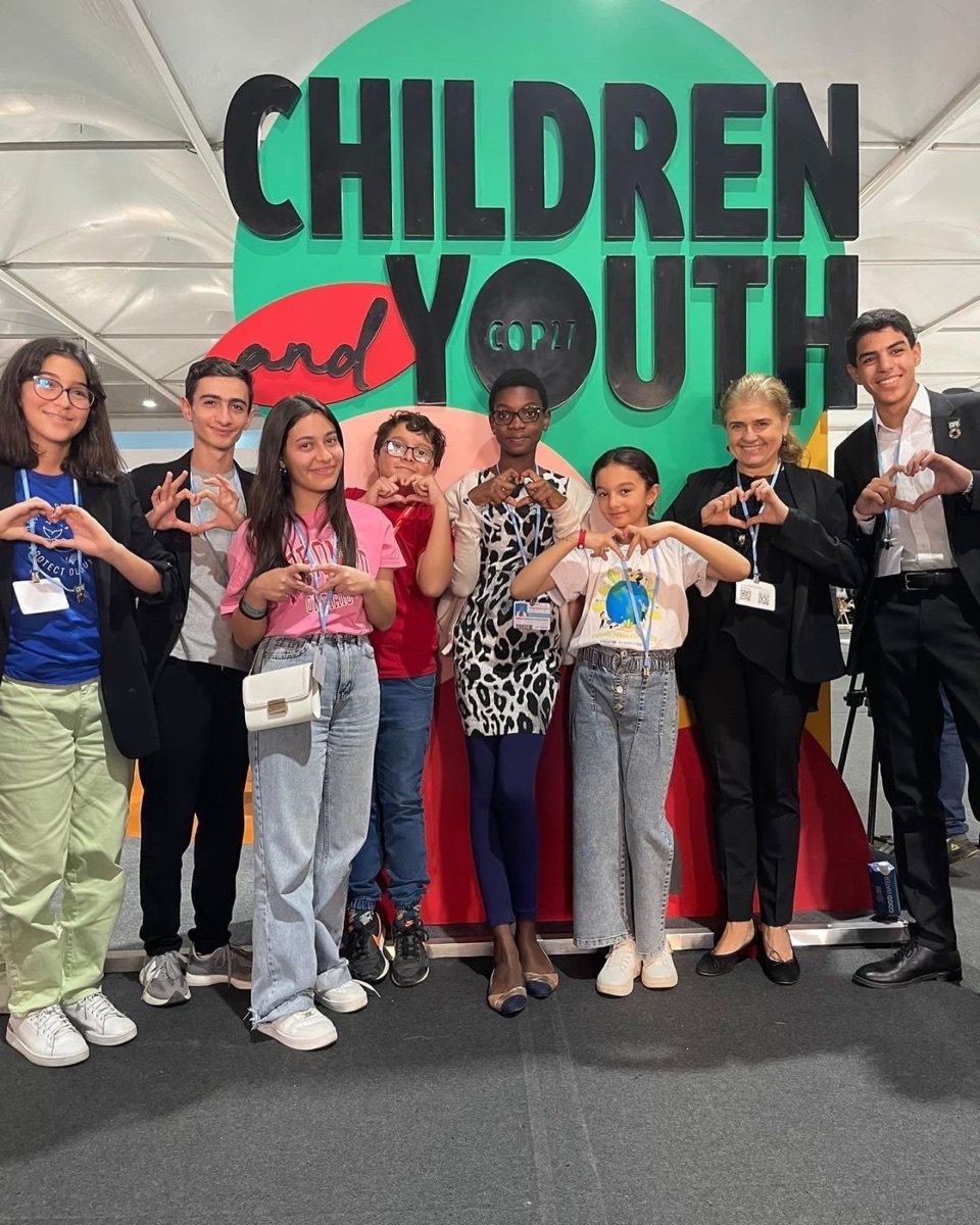 Young delegates forming heart shapes with their hands in front of the Children and Youth pavilion backdrop at COP27