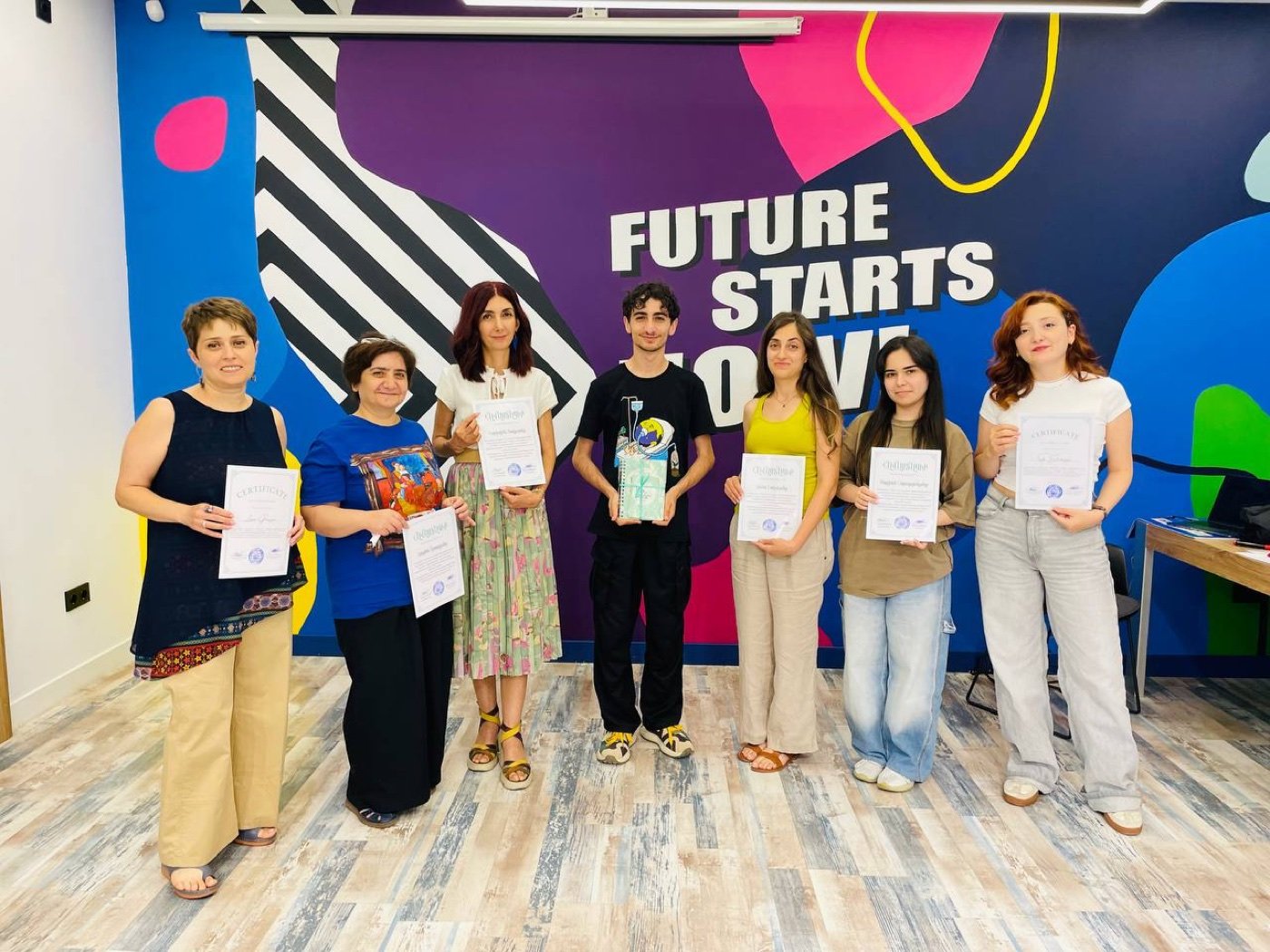 Seven Green Training of Trainers participants holding their certificates in front of a mural reading Future Starts Now